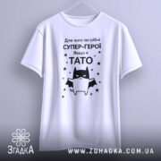 Футболка є тато, білого кольору, зображена в анфас на манекені, фон світло-сірий, принт чорного кольору з зображенням кота-супергероя та текстом на українській мові.