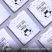 Футболка є тато, білого кольору, зображена в анфас на манекені, фон світло-сірий, принт чорного кольору з зображенням кота-супергероя та текстом на українській мові.
