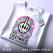 Футболка єдинороги іронія, біла футболка з коротким рукавом, зображена зверху на столі, фон світло-сірий, принт з чорним малюнком руки з середнім пальцем, оточений кольоровими елементами, включаючи райдугу та єдинорогів, на футболці є етикетка.