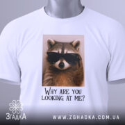 Футболка єнот гумор, біла, складена на столі, фон світлий, принт з єнотом у темних окулярах та текстом 'Why are you looking at me?', з етикеткою на комірці.