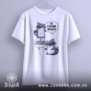 Футболка єнот пердун білого кольору, зображена з фронтального ракурсу на вішалці, фон світло-сірий. Принт з двома єнотами в окулярах, текст аналогічний попереднім зображенням.