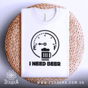 Футболка індикатор пива, біла, складена на плетеному кошику, фон світло-сірий, принт з індикатором рівня пива та написом 'I NEED BEER' чорного кольору.