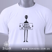 Футболка інопланетянин, біла, зображена зверху на плоскості, фон світло-сірий, принт чорного кольору з інопланетянином, що тримає табличку з написом 'I DON'T BELIEVE IN HUMANS', на футболці є етикетка з логотипом.