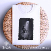 Футболка інопланетна зустріч, біла, складена на плетеній основі, фон світло-сірий, принт з хлопчиком на велосипеді під космічним кораблем, в темних тонах.