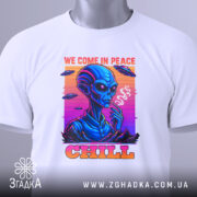 Футболка інопланетний чіл, біла, складена на столі, фон світло-сірий, принт з інопланетянином, який курить, кольори принта яскраві: синій, рожевий, оранжевий, текст 'WE COME IN PEACE' і 'CHILL', на футболці є етикетка з зеленим шнурком.
