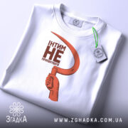 Футболка інтим не пропонувати, біла, зображена на столі, фон світло-сірий, принт з червоним серпом та текстом чорного кольору, на комірці є етикетка.