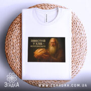 Футболка інвестуй у хліб, складена на плетеній основі, фон білий, принт зображує чоловіка з бородою, який тримає хліб, текст на принті чорний з жовтим.