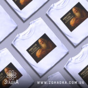 Футболка інвестуй у хліб, білого кольору, зображена на манекені, фон світло-сірий, принт зображує чоловіка з бородою, який тримає хліб, текст на принті чорний з жовтим.