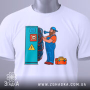 Футболка інженер електрик, біла, зображення зверху, фон світло-сірий, принт з чоловіком у синьому комбінезоні, який працює з електричними проводами, на футболці є етикетка з зеленим шнурком.