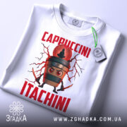 Футболка Itachini Cappuccini білого кольору, зображена з верхнього ракурсу, фон світлий, принт з кавовим стаканом та червоним текстом 'Cappuccini Itachini', на футболці є зелений ярлик.