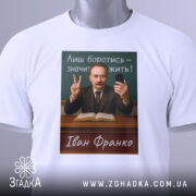 Футболка Іван Франко, біла, складена на поверхні, фон світлий, принт з портретом Івана Франка, текст "Лиш боротись – значить жить!" на зеленому фоні, чоловік у костюмі з бородою, тримає телефон і показує знак миру, на футболці є етикетка.
