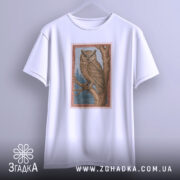 Футболка із совою білого кольору, підвішена на вішалці, ракурс спереду, фон світло-сірий, принт сови на гілці з деталями лісу в блакитному кольорі.