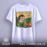 Футболка їжачок оптиміст. Біла футболка, підвішена на вішалці, з принтом їжачка, що тримає кавун. Принт розташований на грудях, фон з зеленими пагорбами та блакитним небом, яскраві кольори.