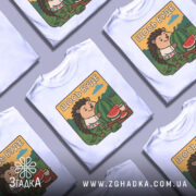 Футболка їжачок оптиміст. Біла футболка з принтом їжачка, що тримає кавун, на фоні зелених пагорбів та блакитного неба. Принт яскравий, з веселим виразом обличчя їжачка, одягнутого в вишиванку.