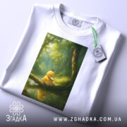 Футболка каченя у лісі, біла, складена, з принтом каченя на гілці, фон з лісом та відображенням у воді, з етикеткою на комірці.