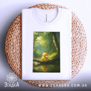 Футболка каченя у лісі, біла, складена на плетеній кошику, з принтом каченя на гілці, фон з лісом та м'яким світлом.