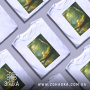 Футболка каченя у лісі, біла, зображення каченя сидить на гілці біля води, фон з зеленими деревами та м'яким світлом.