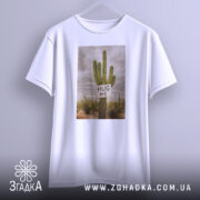 Футболка кактус обійми, біла, підвішена на вішалці, зображена з фронтального ракурсу, фон сірий, принт з кактусом та написом 'HUG ME'.