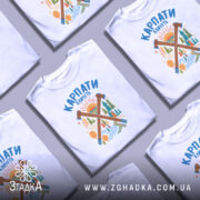 Футболка Карпати кличуть подарунок, біла футболка на манекені, фон світло-сірий, принт з зображенням лісу, сонця та інструментів, яскраві кольори принта.