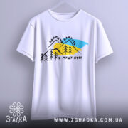 Футболка Карпати кличуть, біла, підвішена на вішалці, фон світло-сірий, принт з горами, деревами та текстом, виглядає стильно.