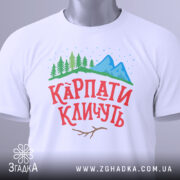 Футболка карпати кличуть, білого кольору, зображена на манекені з фронтального ракурсу, фон світло-сірий, принт з горами, лісом та написом червоного кольору.