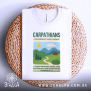 Футболка Карпати Україна, біла, складена на плетеній основі, фон натуральний, принт з горами, сонцем і будинком, текст з назвою Карпат.