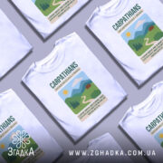 Футболка Карпати Україна, біла, зображена на манекені, фон нейтральний, принт з горами, сонцем і будинком, текст з назвою Карпат.