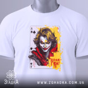 Футболка карта хаосу, біла, зображена на столі, ракурс зверху, фон світло-сірий, принт з обличчям персонажа, яскраві кольори жовтого та червоного, на комірці етикетка з логотипом.