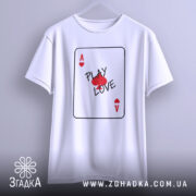Футболка карта кохання, білого кольору, підвішена на вішалці, фон світло-сірий, принт у вигляді картки з написом 'PLAY LOVE' та червоними сердечками.
