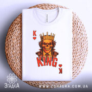 Футболка карта короля, біла, з верхнього ракурсу, на фоні плетеного кошика, складена, принт з черепом у короні, червоний напис 'KING' та символи 'K' і серце.