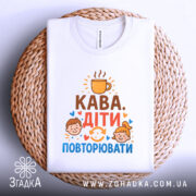 Футболка кава діти повторювати. Біла футболка, складена на плетеній основі, зображена зверху. Принт містить текст 'Кава. Діти. Повторювати' з ілюстраціями дітей та чашки кави, фон білий.