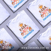 Футболка кава діти повторювати. Біла футболка з коротким рукавом, зображена з фронтального ракурсу на манекені. На фоні світло-сірий колір. Принт містить текст 'Кава. Діти. Повторювати' у яскравих кольорах, з ілюстраціями двох дітей і чашки кави.