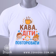 Футболка кава діти повторювати. Біла футболка з круглим вирізом, зображена зверху на білому фоні. На футболці видно принт з текстом 'Кава. Діти. Повторювати' та ілюстраціями дітей. На футболці є етикетка з зеленим шнурком.