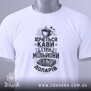 Футболка кава мільйони доларів, біла, складена на поверхні, фон світлий, принт чорного кольору з малюнком чашки кави та грошима, на комірці є етикетка.