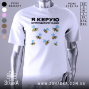 Футболка керую бджілочками, білого кольору, зображена на манекені з правого ракурсу, фон світло-сірий, принт з бджолами та написом "Я КЕРУЮ ЦИМИ БДЖІЛОЧКАМИ" в чорному кольорі.