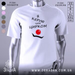 Футболка керую цирком білого кольору, зображена на манекені, з принтом чорного кольору, що містить текст "Я керую цим цирком" та червоний круг, на фоні світло-сірого градієнту.