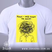 Футболка хаос мій план, біла, розкладена на поверхні, фон світло-сірий, принт з жовтим фоном і чорним малюнком, що зображає людину з заплутаним волоссям, з етикеткою на рукаві.