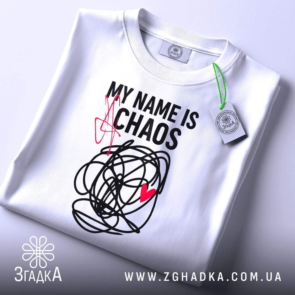 Футболка хаос настрій, біла, складена на поверхні, фон світло-сірий, принт чорний з червоним серцем та написом 'MY NAME IS CHAOS', видно етикетку з зеленим шнурком.