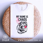 Футболка хаос настрій, біла, складена на плетеній кошику, фон світлий, принт чорний з червоним серцем та написом 'MY NAME IS CHAOS'.