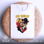 Футболка Харлі Квін білого кольору, складена на плетеній кошику, фон білий. Принт зображає Харлі Квін з двома різними стилями, з написом 'HIS HARLEY' у верхній частині.