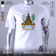 Футболка Хажин білого кольору, зображена на манекені, фон світло-сірий, принт з дерев'яною церквою, річкою та квітами, текст 'KHAZHYN UKRAINE' внизу.