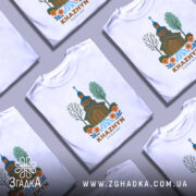 Футболка Хажин білого кольору, зображена на манекені, фон світло-сірий, принт з дерев'яною церквою, річкою та квітами, текст 'KHAZHYN UKRAINE' внизу.