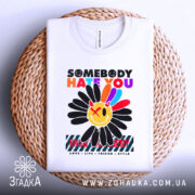 Футболка хейт квітка стиль, біла футболка складена на плетеній кошику, принт квітки яскравий, фон світло-сірий, видно етикетку на горловині.