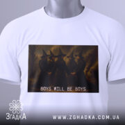 Футболка хлопці магія, біла, складена на столі, фон світлий, принт з чотирма чоловіками в чорних мантіях та капелюхах, текст 'BOYS WILL BE BOYS' під малюнком, на комірці є етикетка.