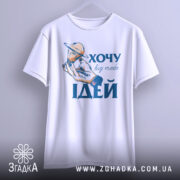 Футболка хочу ідей білого кольору, підвішена на вішалці, фон світло-сірий, принт з рукою, що тримає лампочку з кільцем, текст "ХОЧУ big mebe ІДЕЙ" у синьому кольорі.