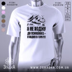 Футболка ходжу в гори, білого кольору, зображена на манекені з правого боку, фон світло-сірий, принт з горами та текстом чорного кольору.