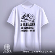 Футболка ходжу в гори, білого кольору, підвішена на фоні світло-сірого кольору, принт з горами та текстом чорного кольору, вид з переду.