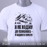 Футболка ходжу в гори, білого кольору, складена на поверхні, фон світло-сірий, принт з горами та текстом чорного кольору, з зеленим ярликом.