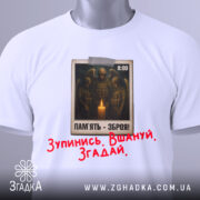Футболка хвилина мовчання. Біла футболка, складена на поверхні, з видимим принтом на грудях. На принті зображені солдати біля свічки, текст "ПАМ'ЯТЬ - ЗБРОЯ!" та червоний напис "Зупинись. Вшануй. Згадай.". Видно етикетку з зеленим шнурком.