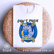 Футболка кінь боксер не жени, біла футболка складена на плетеному кошику, ракурс зверху, фон світло-сірий, принт з зображенням коня в боксерських рукавичках, текст 'DON'T PUSH THE HORSES' жовтого кольору, деталі принта в синіх та жовтих відтінках.